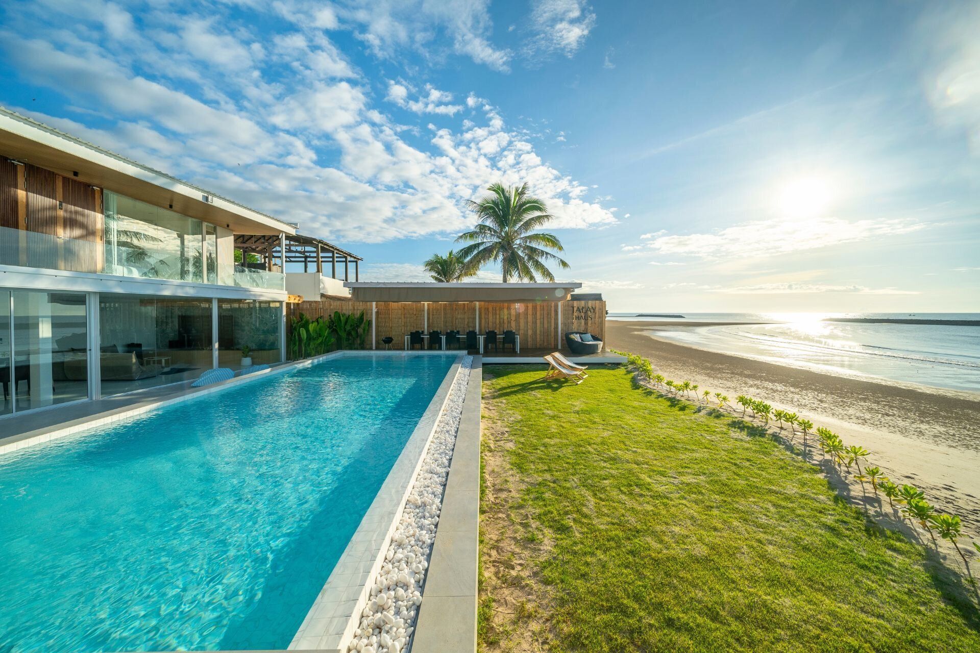 Beachfront pool at Talay Haus X Pool Villa, Cha-am, Phetchaburi. View of the pool, lawn, beach, and ocean.