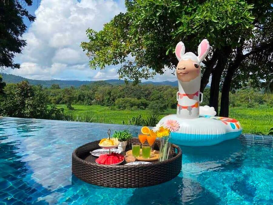 Floating breakfast with fresh fruit and drinks in the infinity pool at The Valley Khaoyai I, overlooking lush green fields.