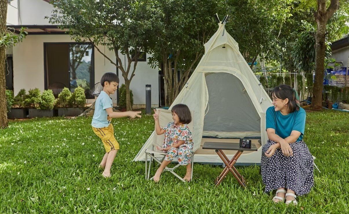 A family enjoys outdoor play with a tent in the lush garden of The Valley Khaoyai I pool villa in Khao Yai.