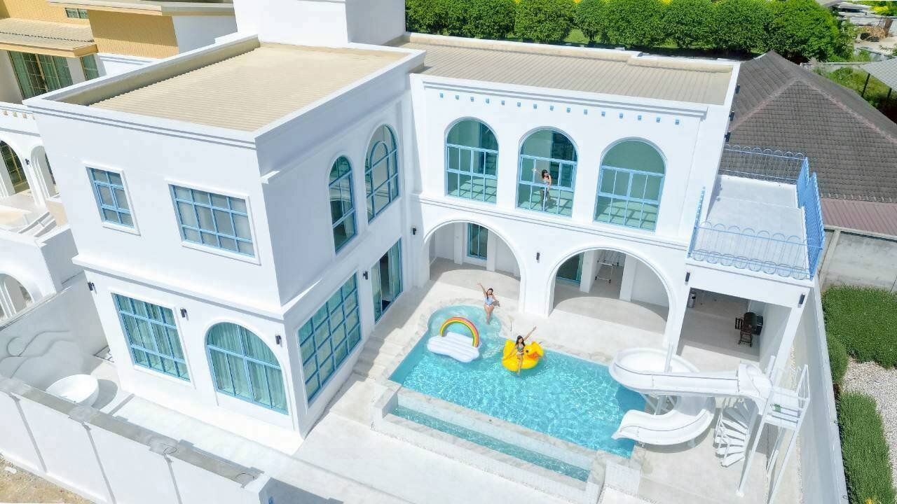 Aerial view of Tierra V Pool Villa in Pattaya, showcasing the white exterior, private pool with slide, and guests enjoying the water.