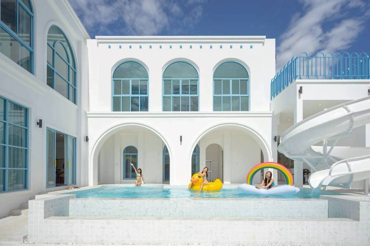 Guests enjoy the large swimming pool with a water slide at Tierra V Pool Villa in Pattaya, Thailand.