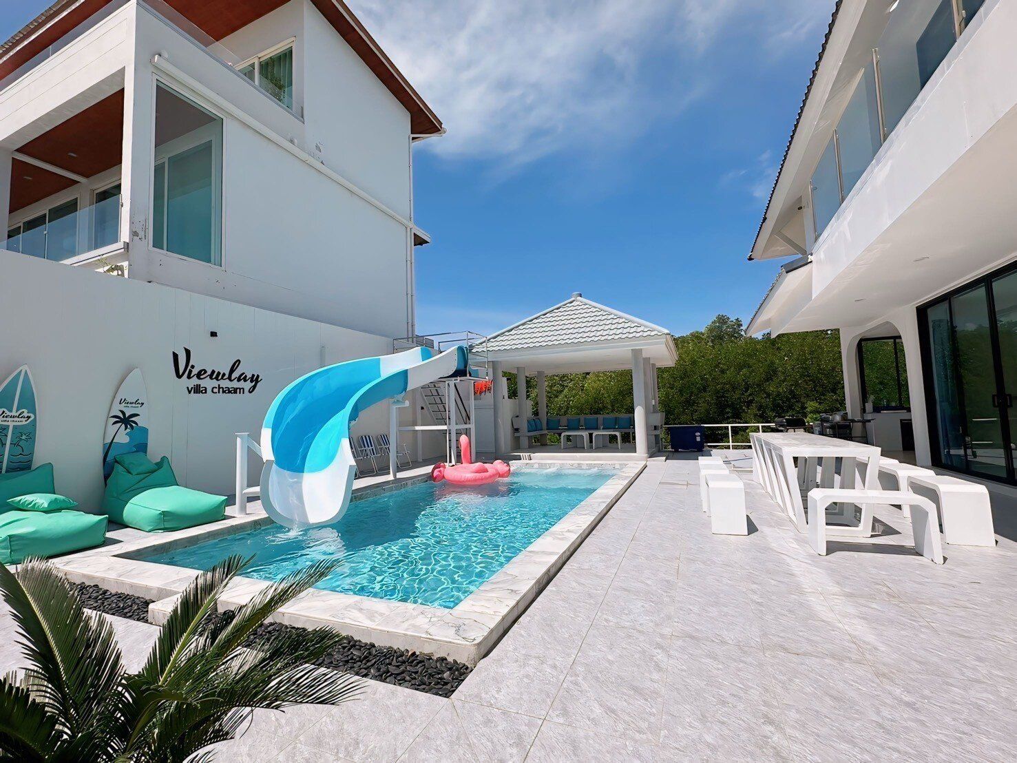 View Lay IV Pool Villa in Cha-Am features a refreshing outdoor pool with a fun blue and white water slide and a pink flamingo float.