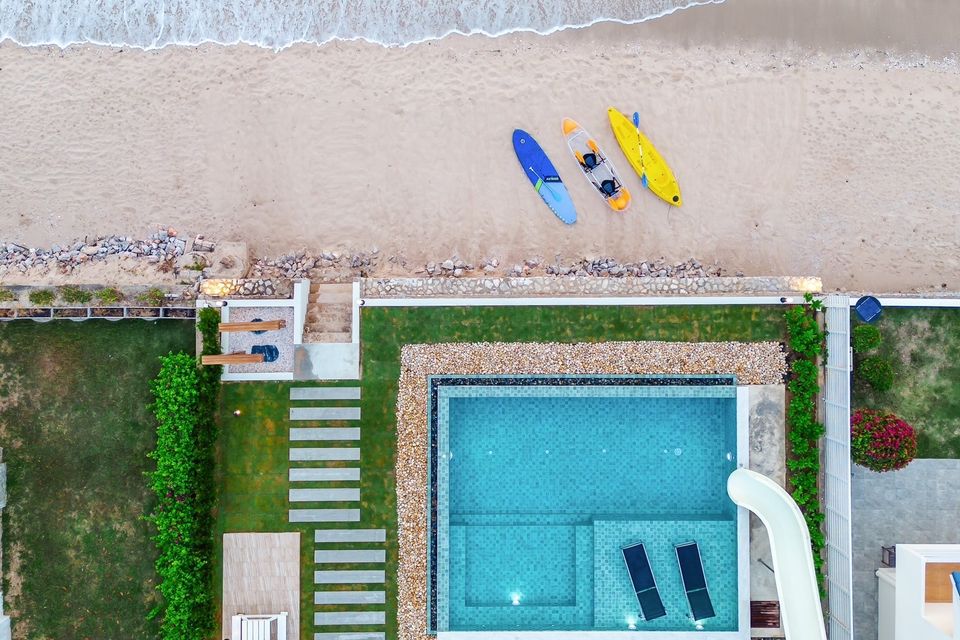 Aerial view of All About VII Pool Villa near Bangket Beach, Cha-am. Kayaks on the sand, pool with slide and sun loungers.