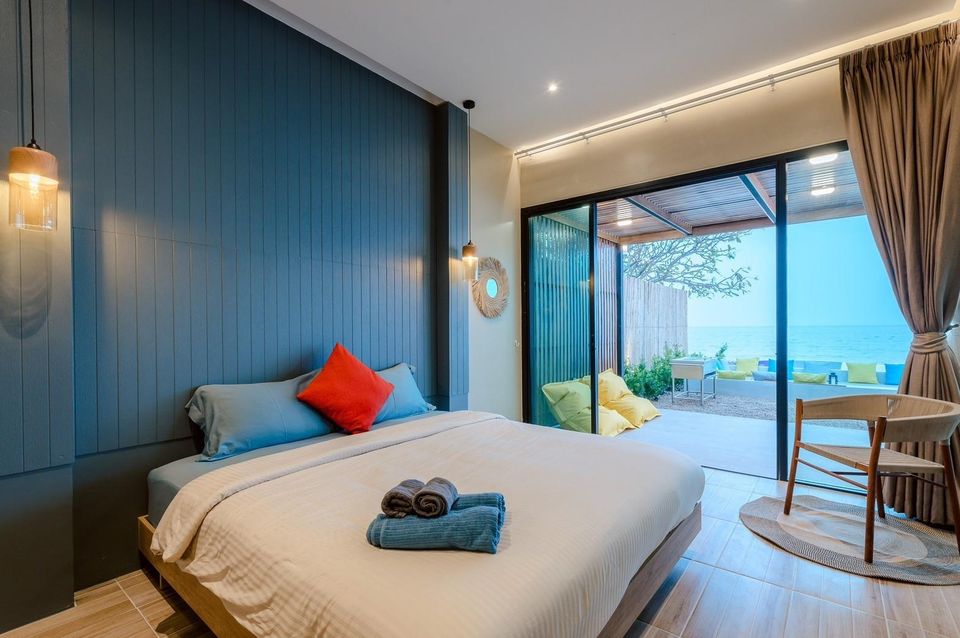 King-size bed with blue and red pillows in a bedroom at Beach Blanca IV Pool Villa, Cha-Am, offering direct ocean views.