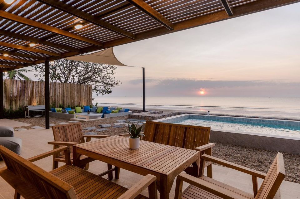 Outdoor dining table at Beach Blanca IV Pool Villa, Cha-Am. View of the pool and ocean at sunset.