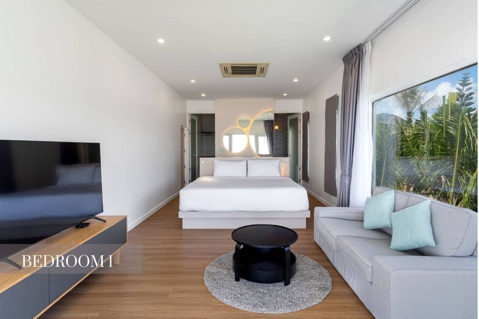 Spacious bedroom at Caribbean V Pool Villa, Hua Hin, featuring a king-size bed, sofa, TV, and large window with lush views.