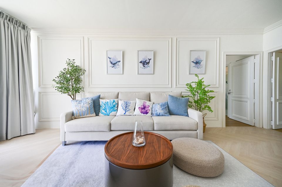 Bright living room at Coastal Calm IV Pool Villa, Cha-Am, with a light sofa, blue and coral pillows, and whale art.