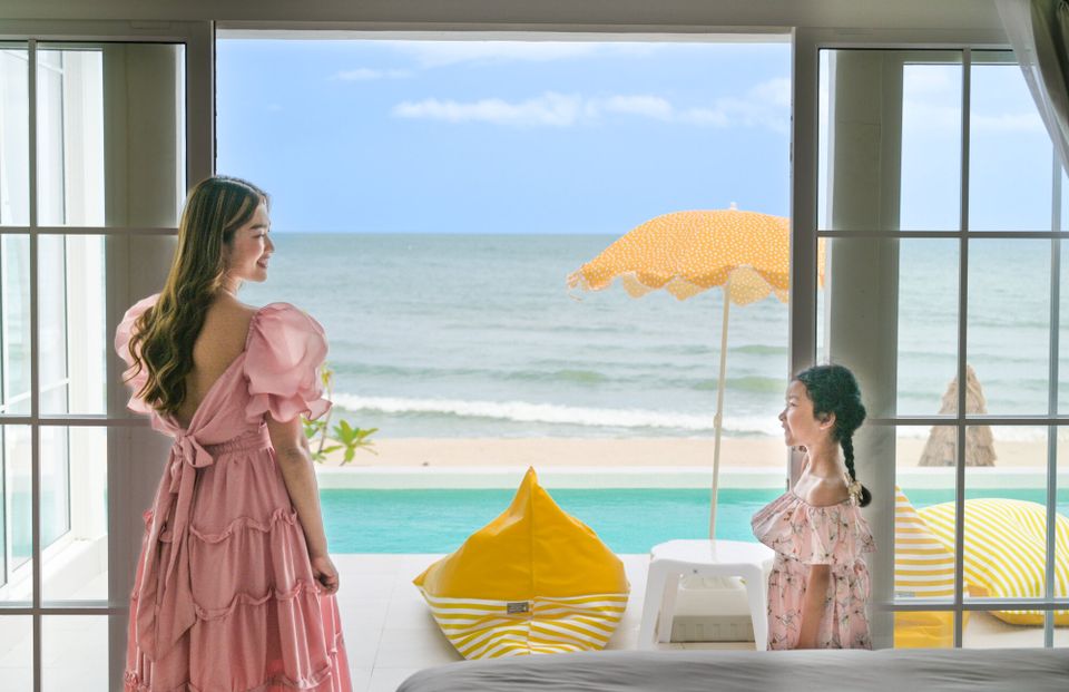A woman and child look out from a bedroom balcony at Coastal Calm IV Pool Villa, Cha-Am, with an infinity pool and ocean vie