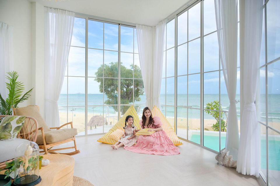 Coastal Calm IV pool villa living area with ocean view. Mother and daughter sit by the window.
