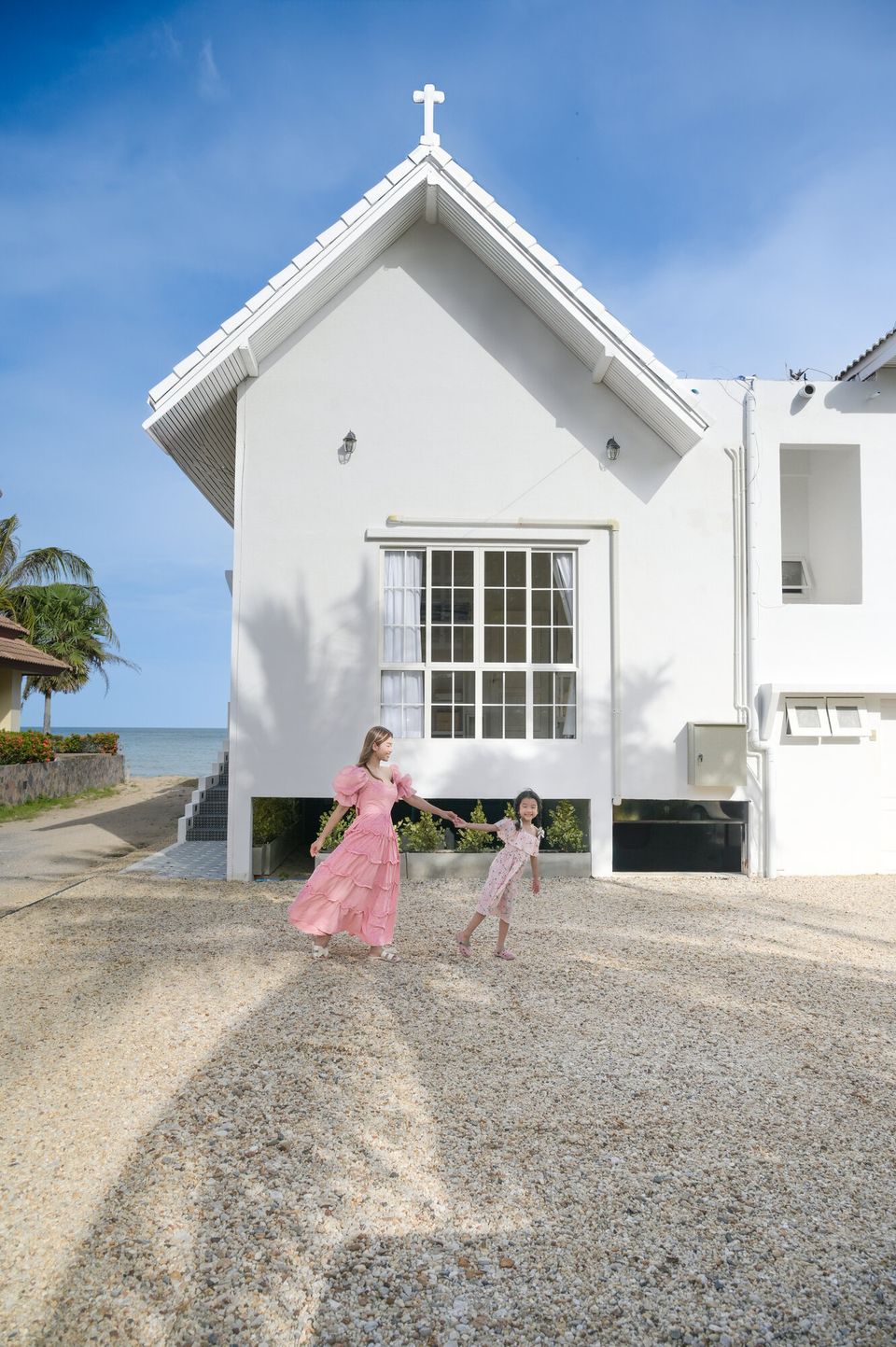 Coastal Calm IV Pool Villa in Cha-Am: A mother and child walk on the gravel driveway in front of the white beachfront villa.