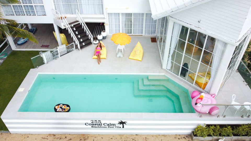 Aerial view of the pool at Coastal Calm IV Pool Villa. Woman relaxing on a yellow beanbag by the pool.