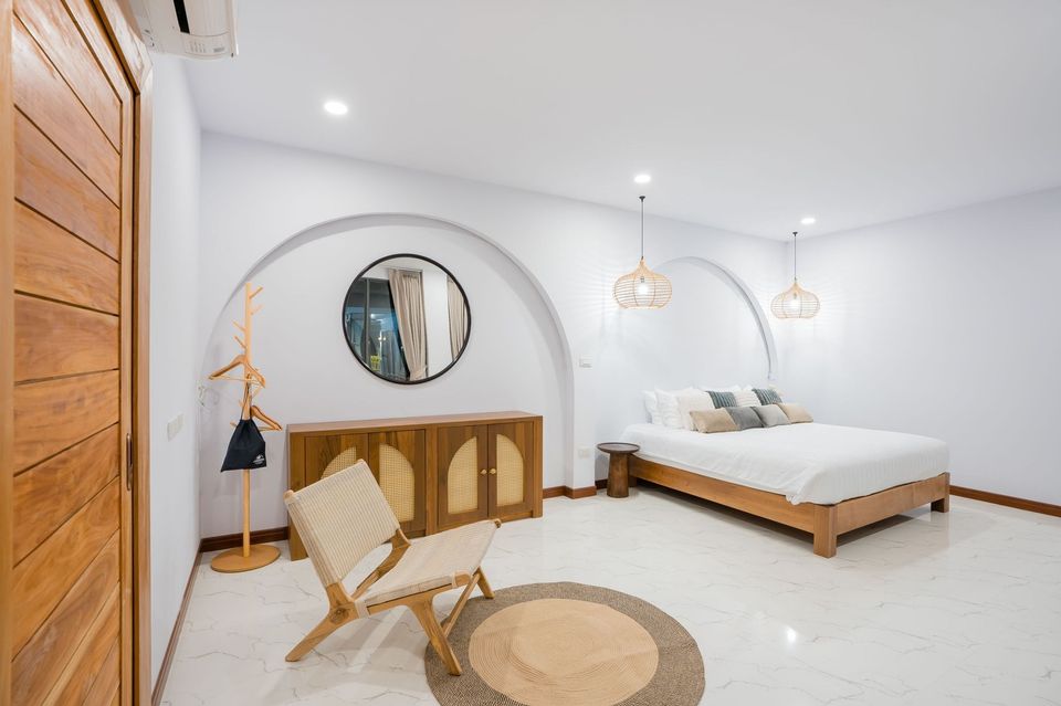 Cross Sea VII Pool Villa bedroom in หาดคลองเทียน-ชะอำ features a king bed, round mirror, and woven chair on a round rug.