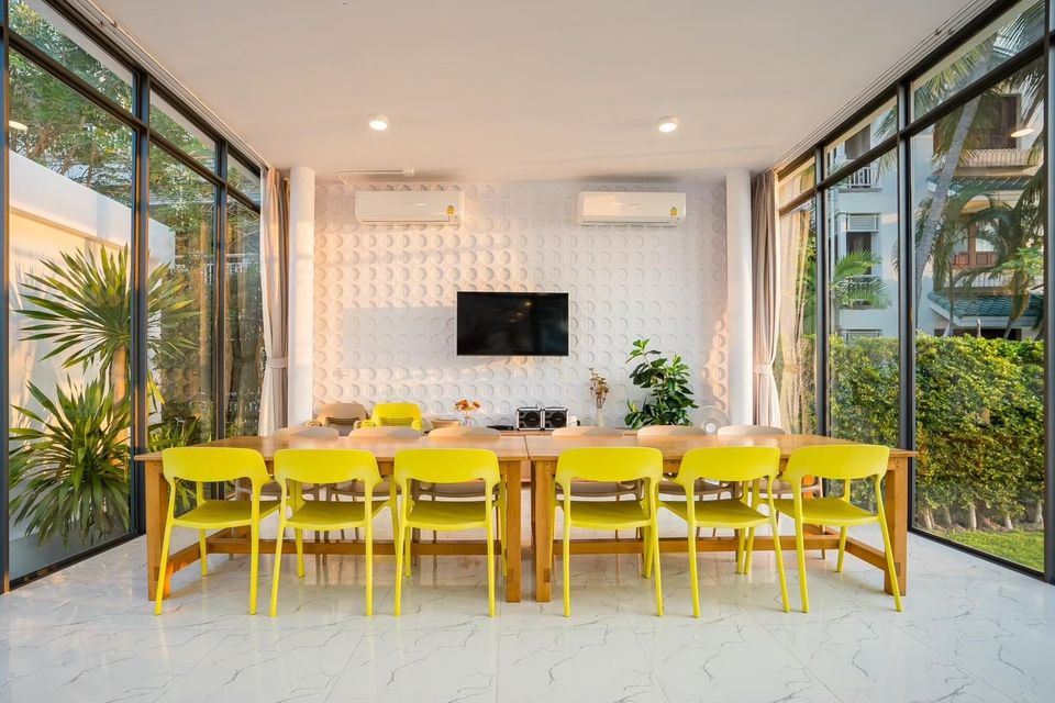 Bright dining area at Cross Sea VII Pool Villa, หาดคลองเทียน-ชะอำ. Long wooden table with yellow chairs, TV, and large window