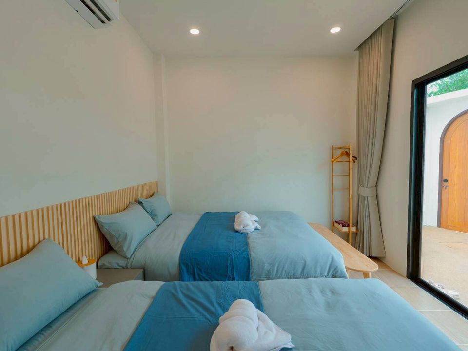 Bright bedroom at Darlington IV Pool Villa, Cha-Am, featuring two comfortable twin beds with blue linens and a balcony door.