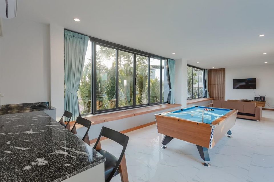 Exclusive Proud VII Villa in Hua Hin features a bright living area with a billiards table, bar seating, and large windows.