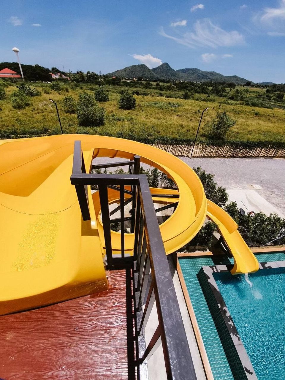Bright yellow spiral water slide at Exclusive Proud VII Villa in Hua Hin, leading into a refreshing pool with mountain views.