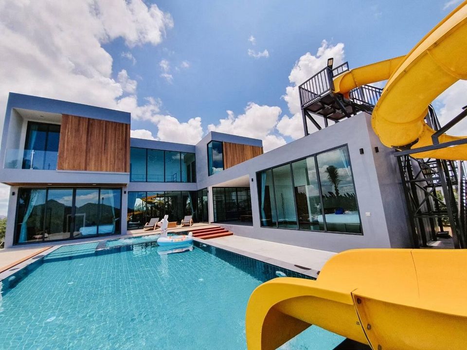 Exclusive Proud VII Villa in Hua Hin features a large private pool with an exciting yellow water slide under a blue sky.