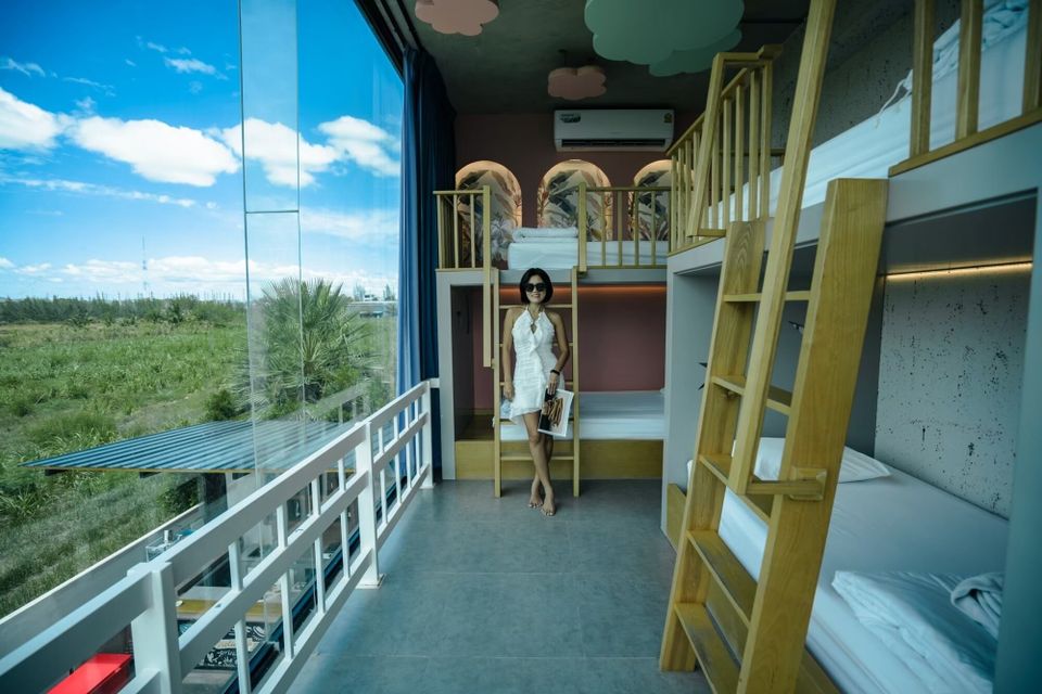 A woman stands in a modern bunk bed room at Holiday Sunset Villa IV, Hua Hin, with a large window overlooking greenery.