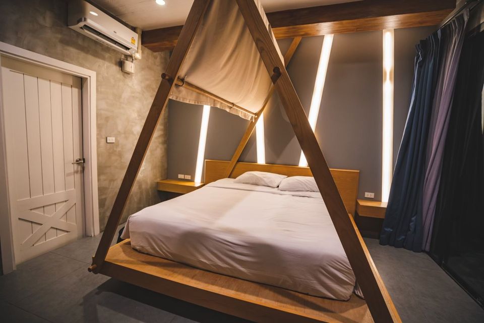 Modern bedroom at Holiday Sunset Villa IV, Hua Hin, featuring a unique wooden canopy king bed with white linens and ambient lighting.