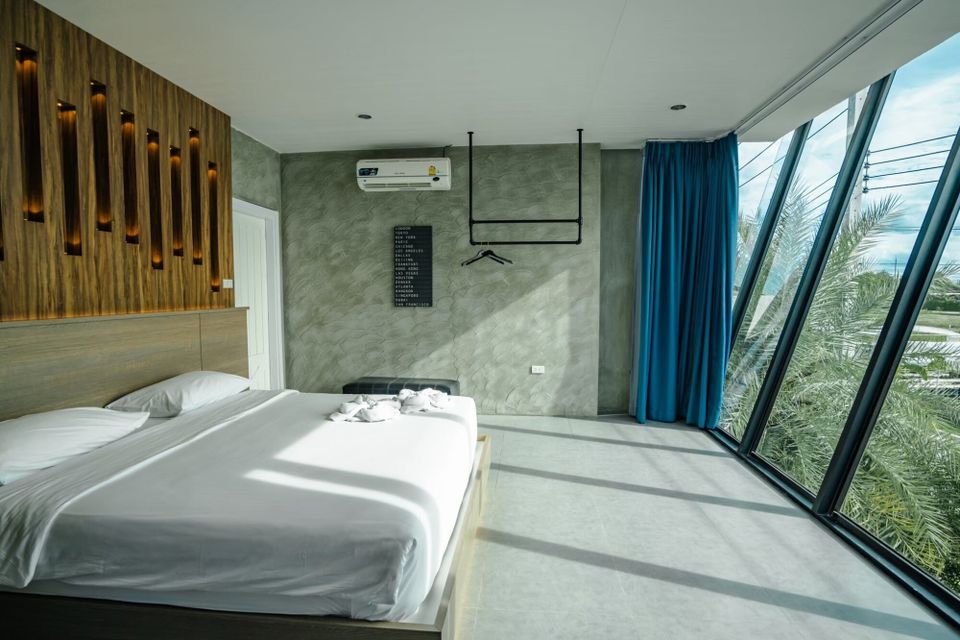 Modern bedroom at Holiday Sunset Villa IV, Hua Hin, with a comfortable bed, wood paneling, and large windows overlooking palm trees.