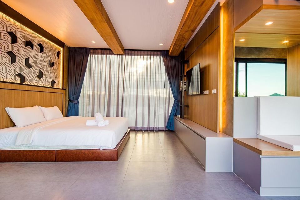 A modern bedroom at Holiday Sunset Villa IV in Hua Hin, featuring a king-size bed, wall-mounted TV, and large windows.
