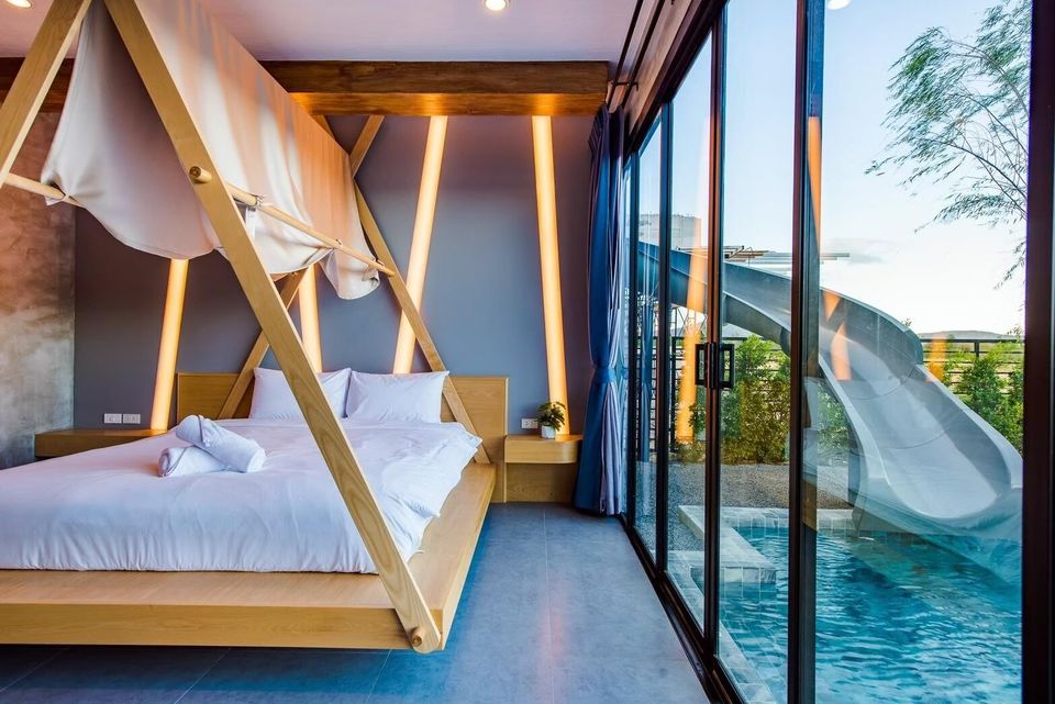 Modern bedroom at Holiday Sunset Villa IV, Hua Hin, with a unique wooden bed frame and direct views of the pool and water slide.