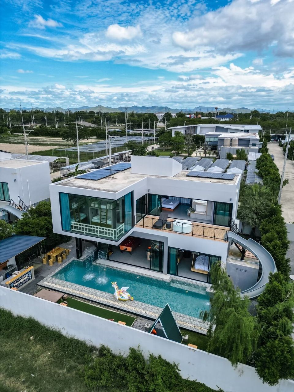 Aerial view of Holiday Sunset Villa IV in Hua Hin, showcasing its modern design, private pool, and surrounding landscape under a blue sky.