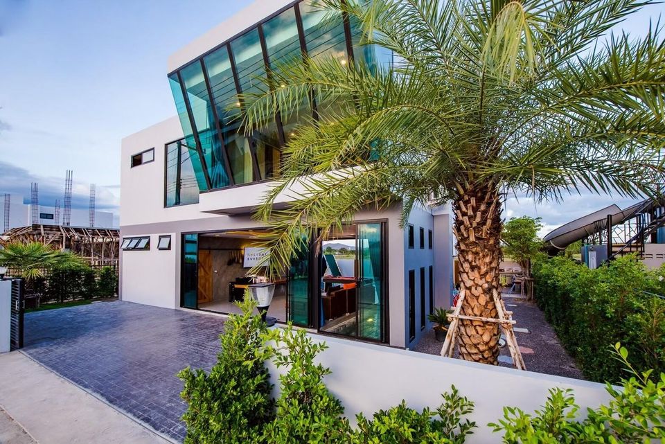 Modern glass facade of Holiday Sunset Villa IV in Hua Hin, featuring a palm tree and clear blue sky.