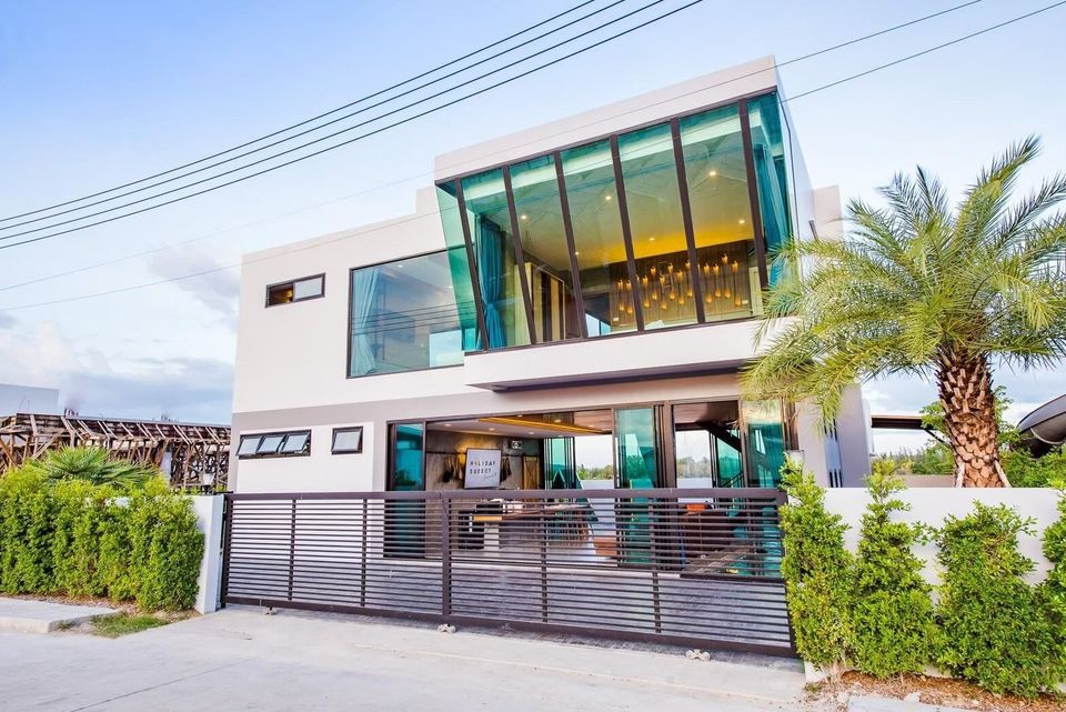 Modern glass facade of Holiday Sunset Villa IV in Hua Hin, featuring a sleek design and lush green landscaping.