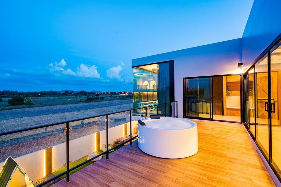 Rooftop jacuzzi on a wooden balcony at Holiday Sunset Villa IV in Hua Hin, with evening sky and distant lights.