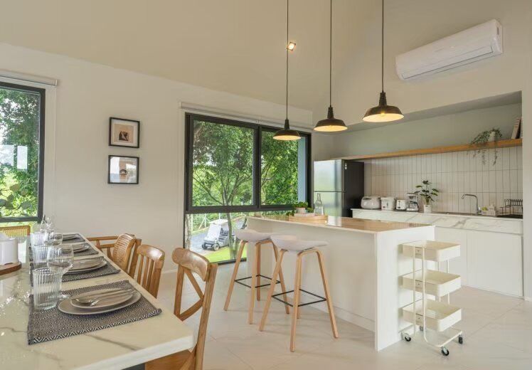 Modern kitchen and dining area at Kin Khaoyai V Pool Villa, Khao Yai, with island seating and lush green views.