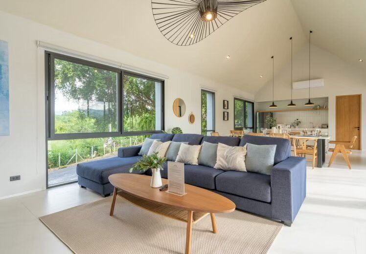 Spacious open-plan living area with a large blue sofa, wooden coffee table, and dining area at Kin Khaoyai V Pool Villa.