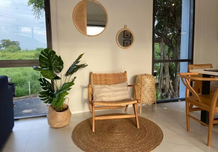 Cozy living area at Kin Khaoyai V Pool Villa with a rattan armchair, round rug, and large windows overlooking greenery.