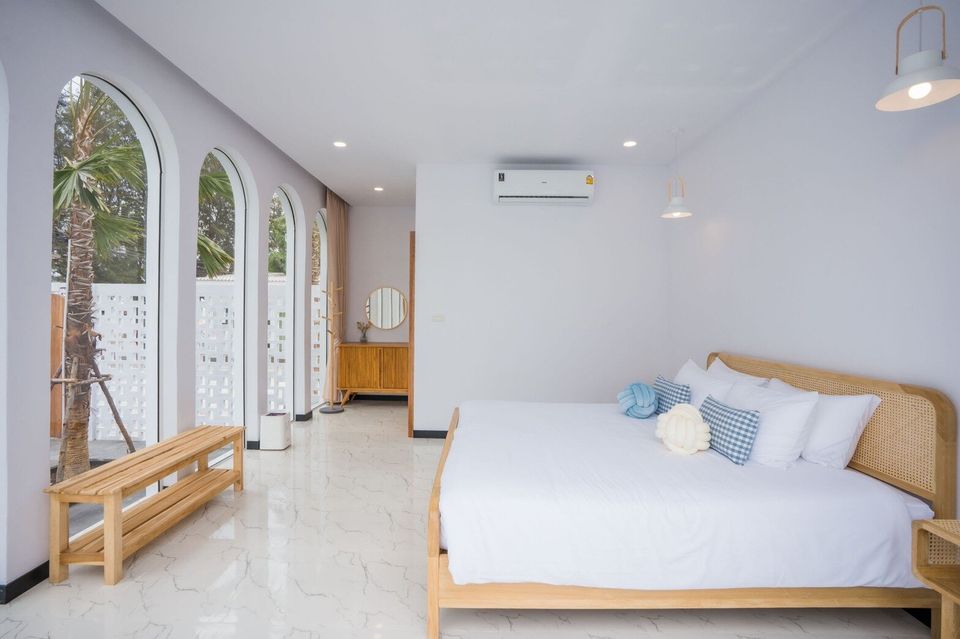 Bright bedroom at Miami Beach VI Pool Villa, Cha-Am, with a king-size bed, arched windows, and a wooden bench.