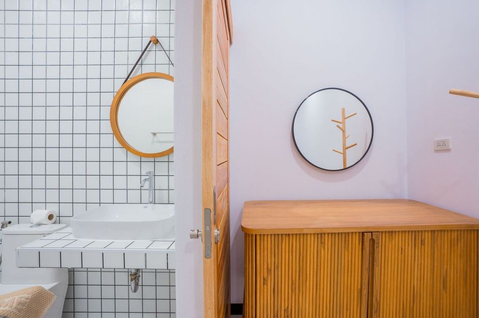 Modern bathroom with white tiled walls, a vessel sink, and a round wooden mirror at Miami Beach VI Pool Villa, Cha-Am.