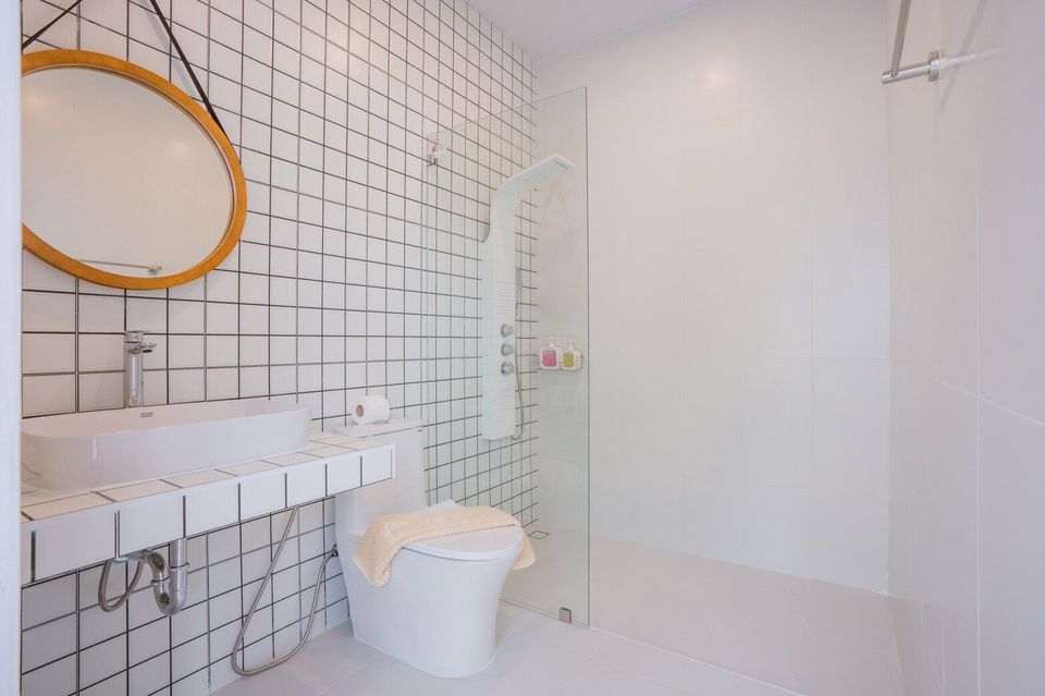 Modern bathroom with white subway tiles, a round wooden mirror, vessel sink, toilet, and walk-in shower at Miami Beach VI Pool Villa, Cha-Am.
