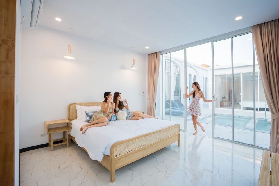 Three women enjoying a bright bedroom with direct pool access at Miami Beach VI Pool Villa, Cha-Am. White decor, rattan bed.