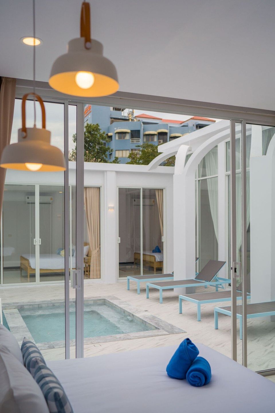 A bedroom at Miami Beach VI Pool Villa in Cha-Am with a view of the private pool and sun loungers through sliding glass doors.