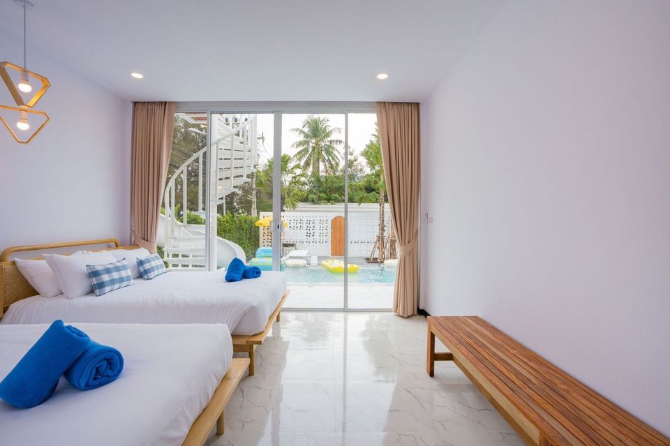 Bright bedroom at Miami Beach VI Pool Villa, Cha-Am, with two beds, blue towels, and direct sliding door access to the pool.