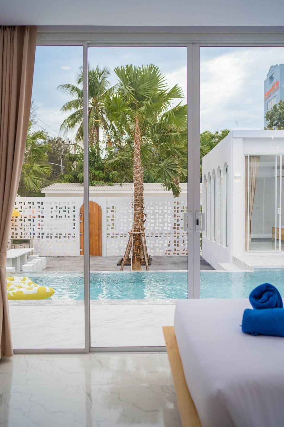 Bedroom with a view of the pool and palm trees at Miami Beach VI Pool Villa in Cha-Am, Thailand.