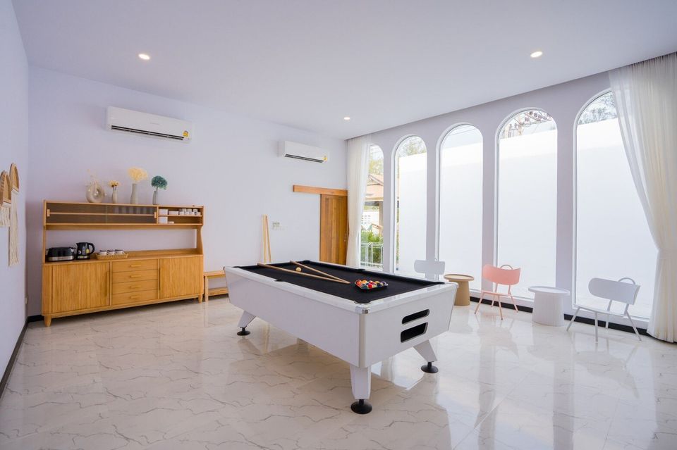 A bright game room with a white billiards table and cue sticks at Miami Beach VI Pool Villa in Cha-Am, Thailand.