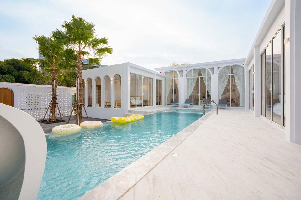 Daytime view of the Miami Beach VI Pool Villa in Cha-Am, featuring a clear blue pool with inflatables and palm trees.