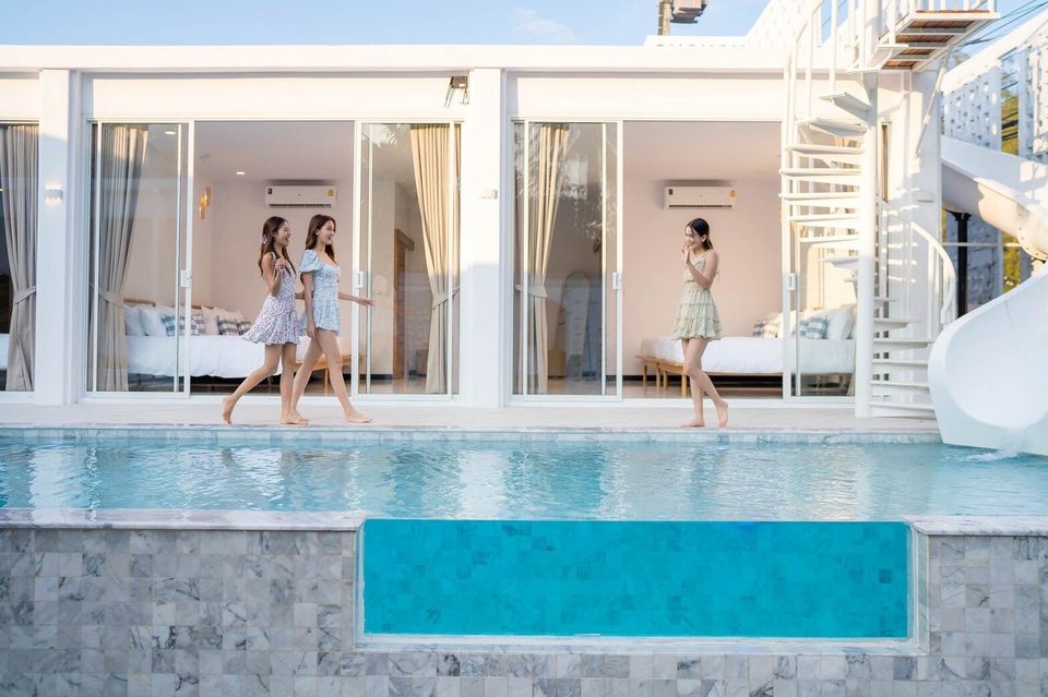 Three women walk along the pool deck of Miami Beach VI Pool Villa in Cha-Am, featuring a unique glass-wall pool.
