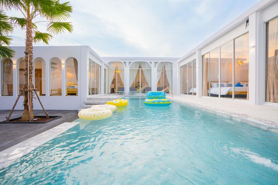 U-shaped swimming pool with yellow and blue inflatables at Miami Beach VI Pool Villa, Cha-Am. Modern white architecture.