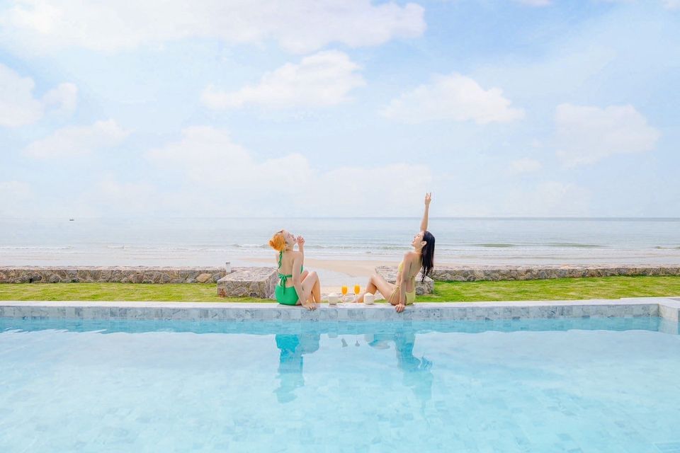 Two women relax poolside at Pailay V Beachfront Pool Villa, ชะอำ เพชรบุรี. Enjoying drinks with ocean views.