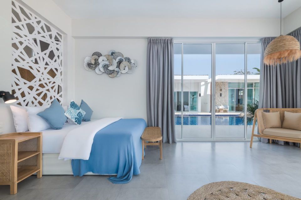 Bright bedroom with pool view at Vela VI Pool Villa, หาดปึกเตียน ชะอำ. King bed, blue accents, and sliding glass doors.