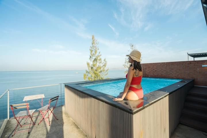 Woman in red swimsuit sits by the rooftop plunge pool at Pink Sand Beachfront Villa, Bang Lamung, North Pattaya. Ocean view.