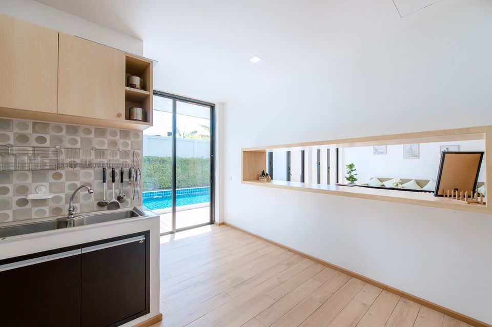 Modern kitchen with pool view at Pool Lay AI Pool Villa, Na Jomtien, Pattaya. Sink, cabinets, and serving hatch.