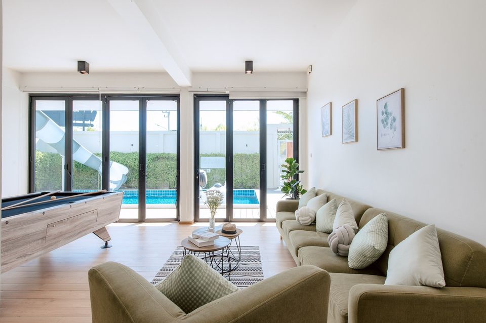 Bright living room at Pool Lay AI Pool Villa, Na Jomtien. Features pool table and view of pool with waterslide.