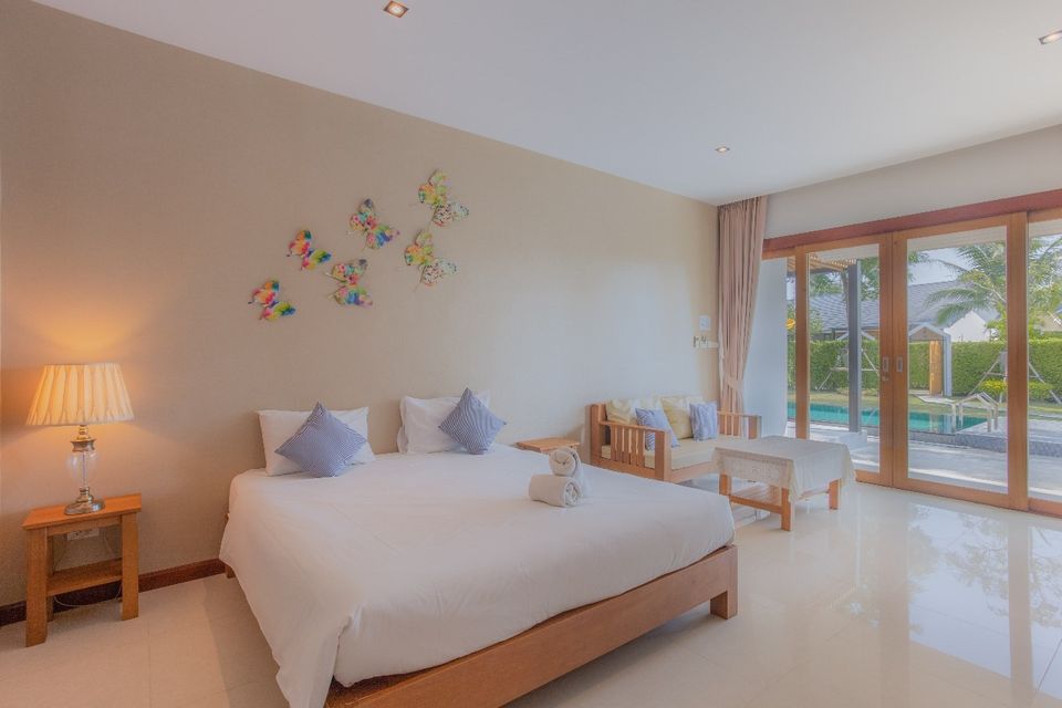 Bright bedroom with pool view at Proud V Pool Villa, Hua Hin. King bed, sofa, and butterfly wall art.